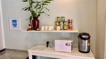 Cozinha com bancada branca, cafeteira, um vaso com planta e diversos recipientes de comida.