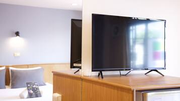 Ett hotellrum med ett skrivbord i trä, en platt-TV på ett stativ, ett nattduksbord med en lampa och en säng med en sänggavel.