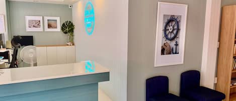 A reception area with a counter, two chairs, framed artwork, and a neon sign.