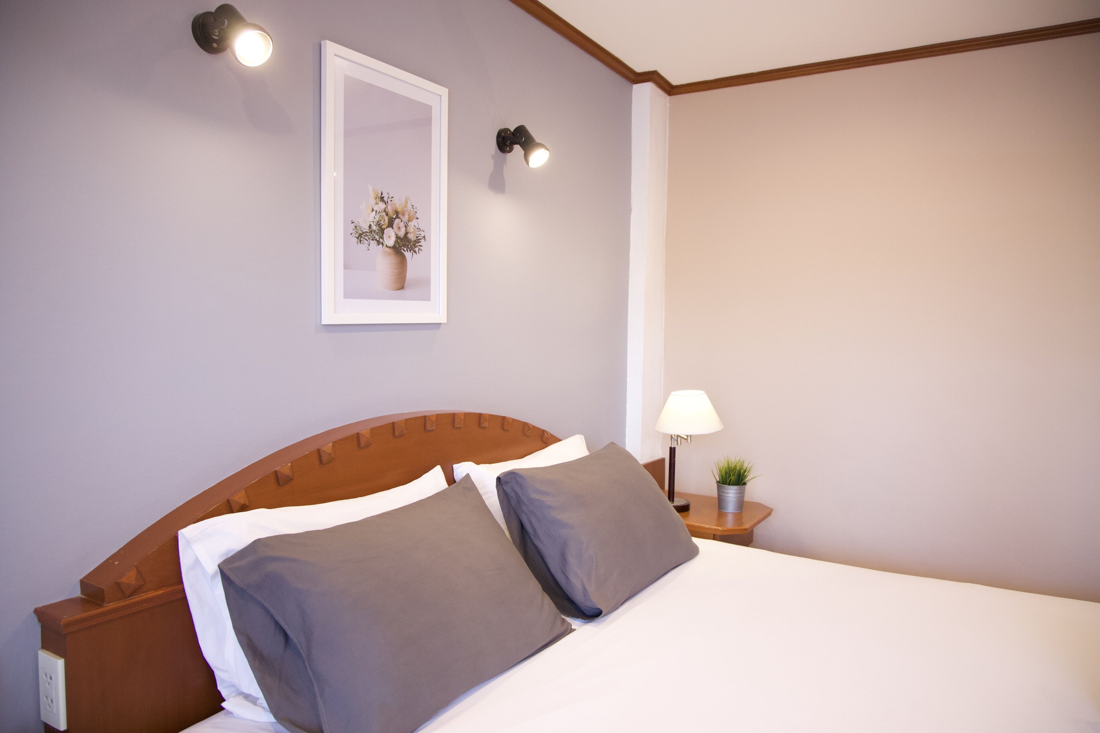 Una cama bien hecha con dos almohadas, una mesita de noche con una lámpara y un cuadro en la pared.
