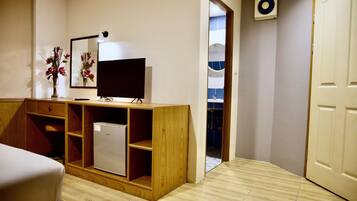 Une chambre de taille modeste, comprenant un lit, un bureau en bois avec une télévision, un petit réfrigérateur et un miroir.