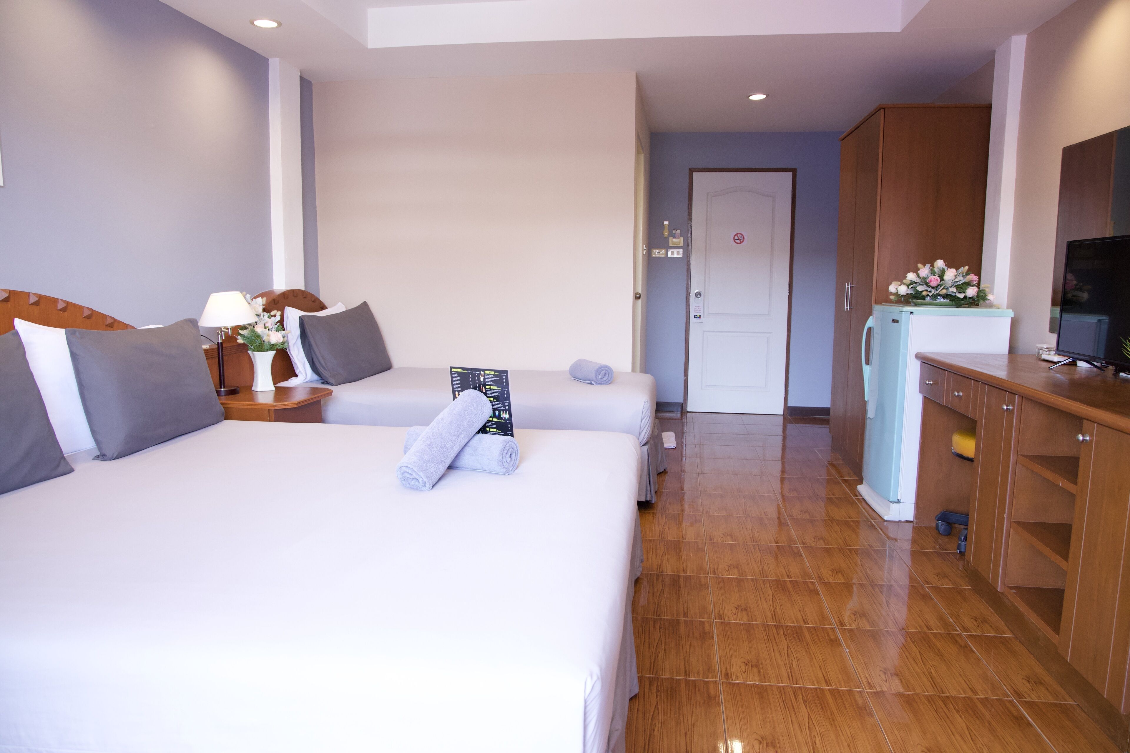 A hotel room with a large bed, a desk with a lamp, a television, and a refrigerator.