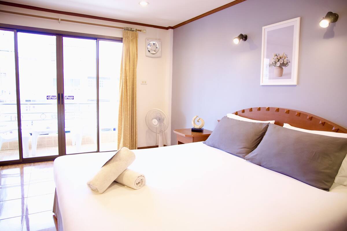A hotel room with a large bed, a fan, a nightstand, and a view through the sliding glass door.