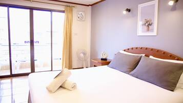 A hotel room with a large bed, a fan, a nightstand, and a view through the sliding glass door.
