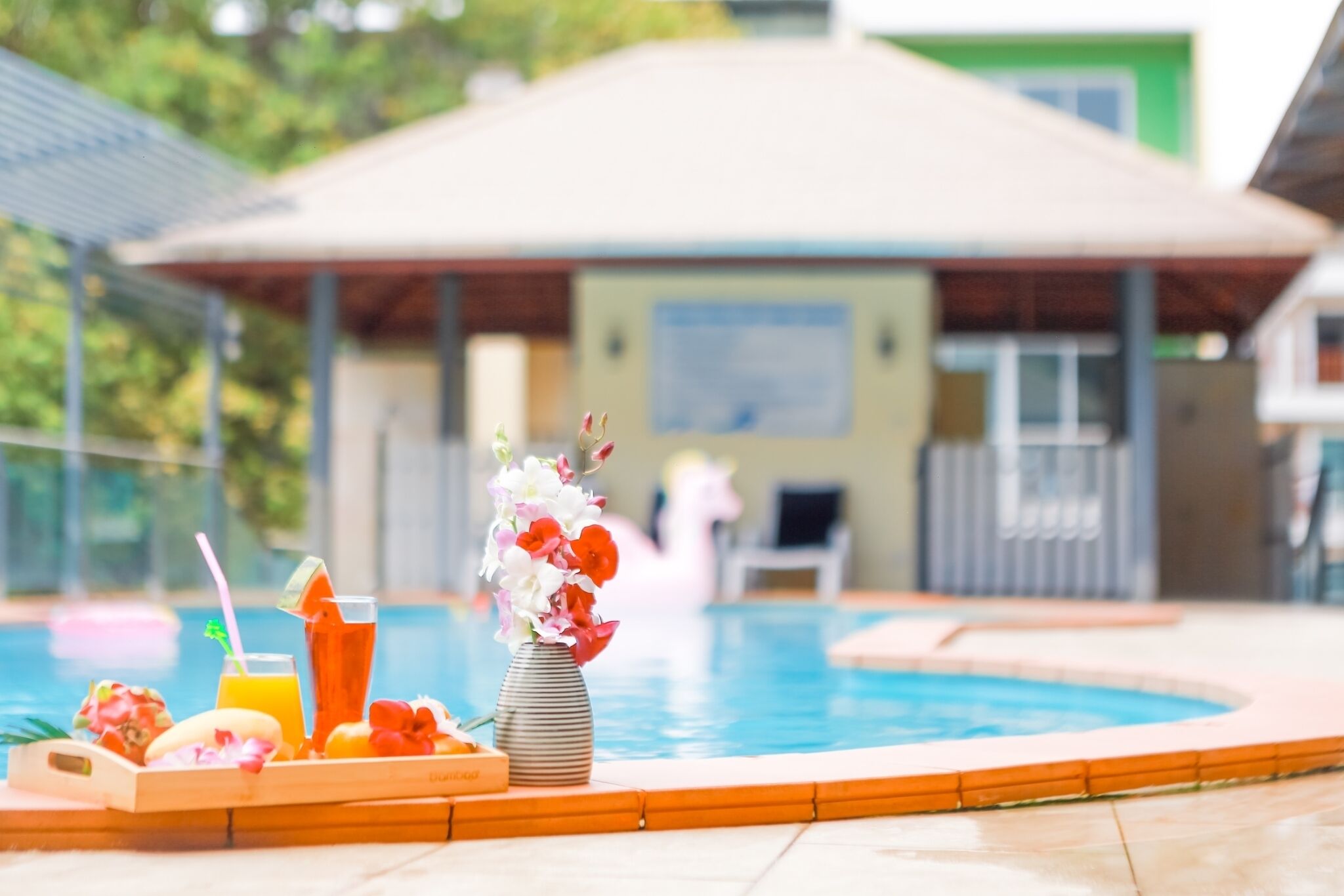 A poolside setting with a drink tray, a vase of flowers, and a pool in the background.