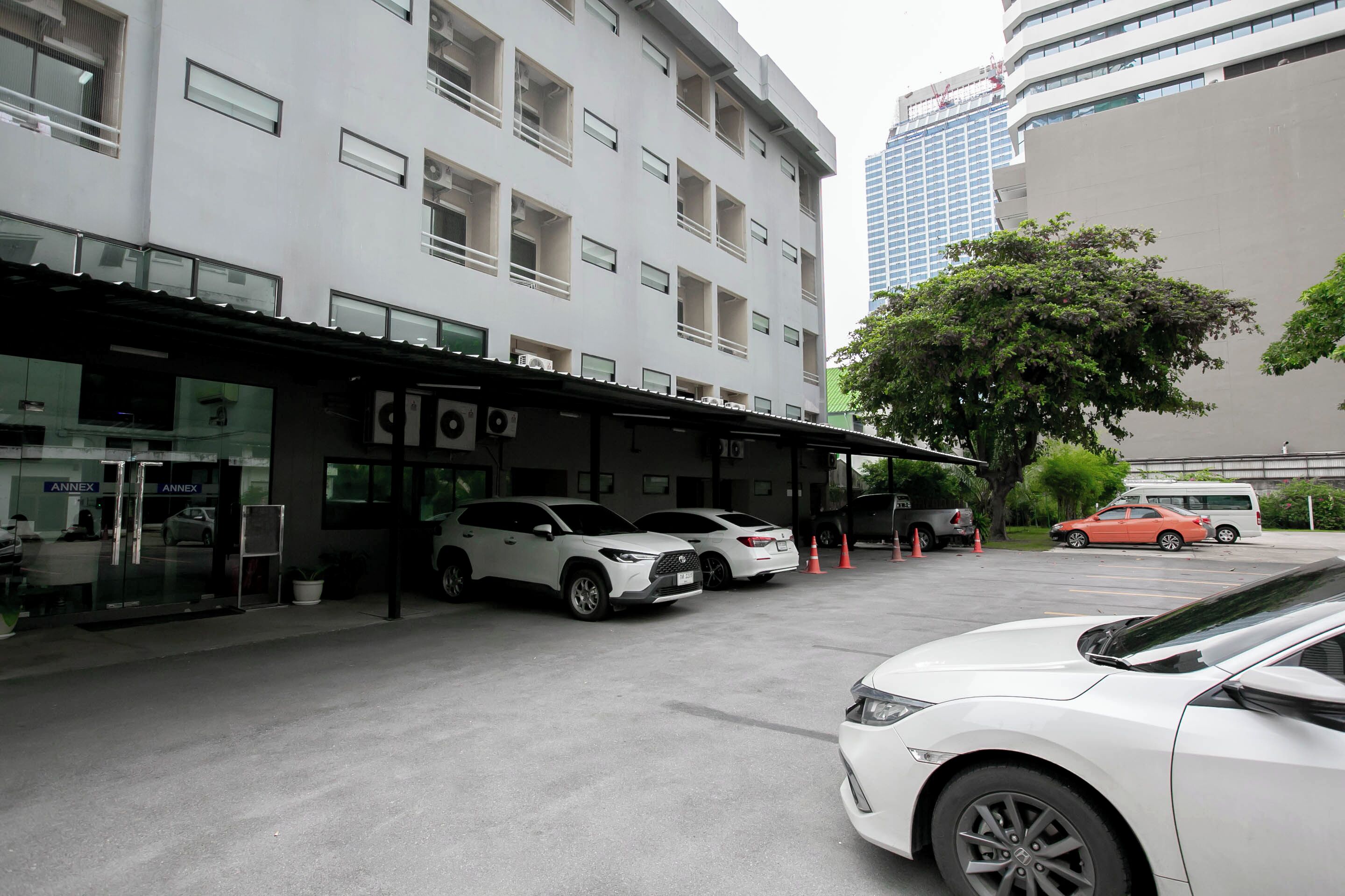 A parking area with white cars, a covered entrance, and a building with multiple floors and windows.