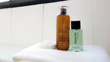 A bathroom with a white towel, a bottle of AETAS conditioning shampoo, and a bottle of Shower Gel.