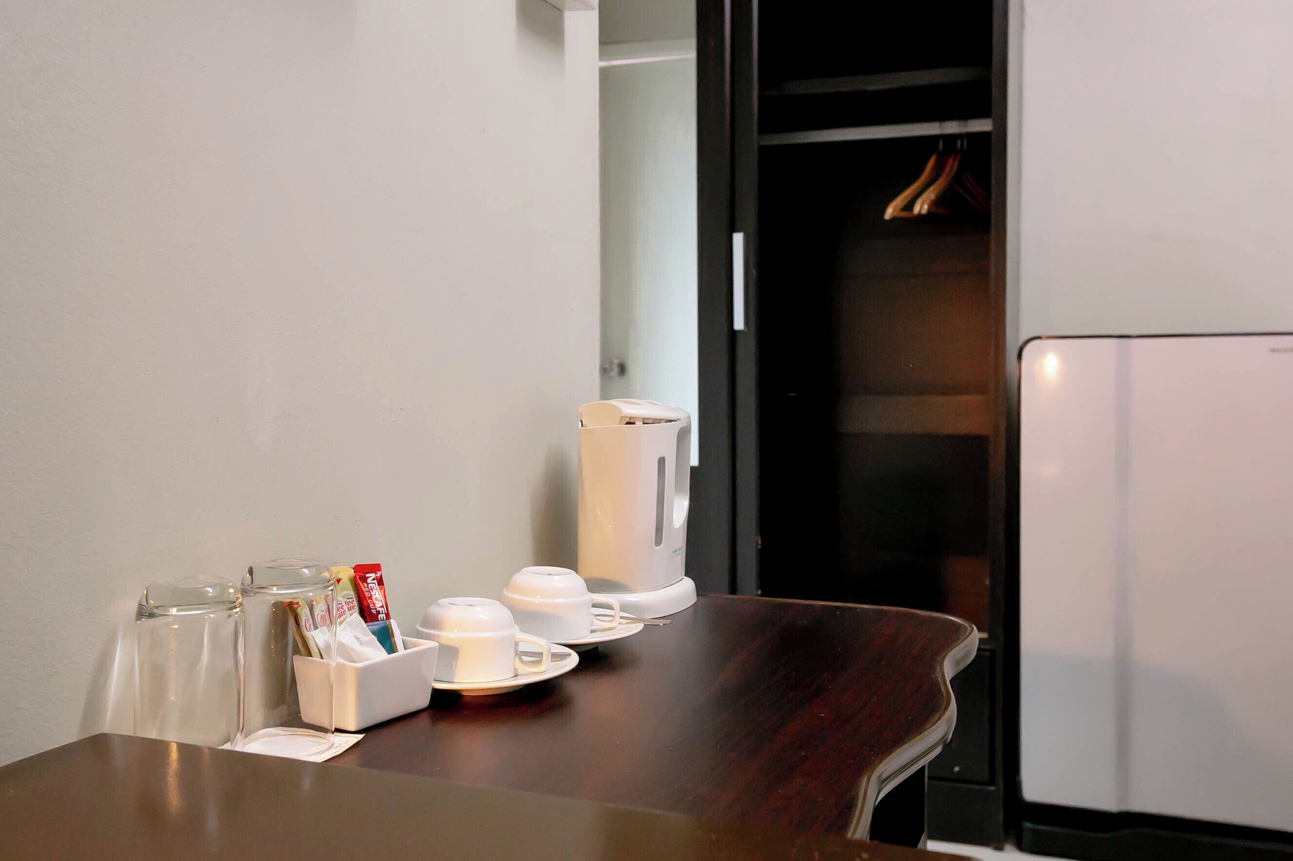 A hotel room with a wooden table, a white coffee maker, and a glass container with cups and a box of tissues.