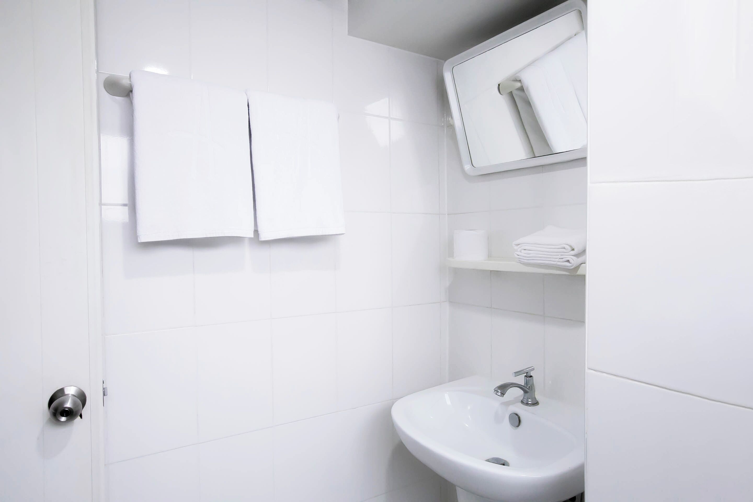 Un baño moderno con azulejos blancos, un lavamanos, un espejo y dos toallas colgadas en la pared.