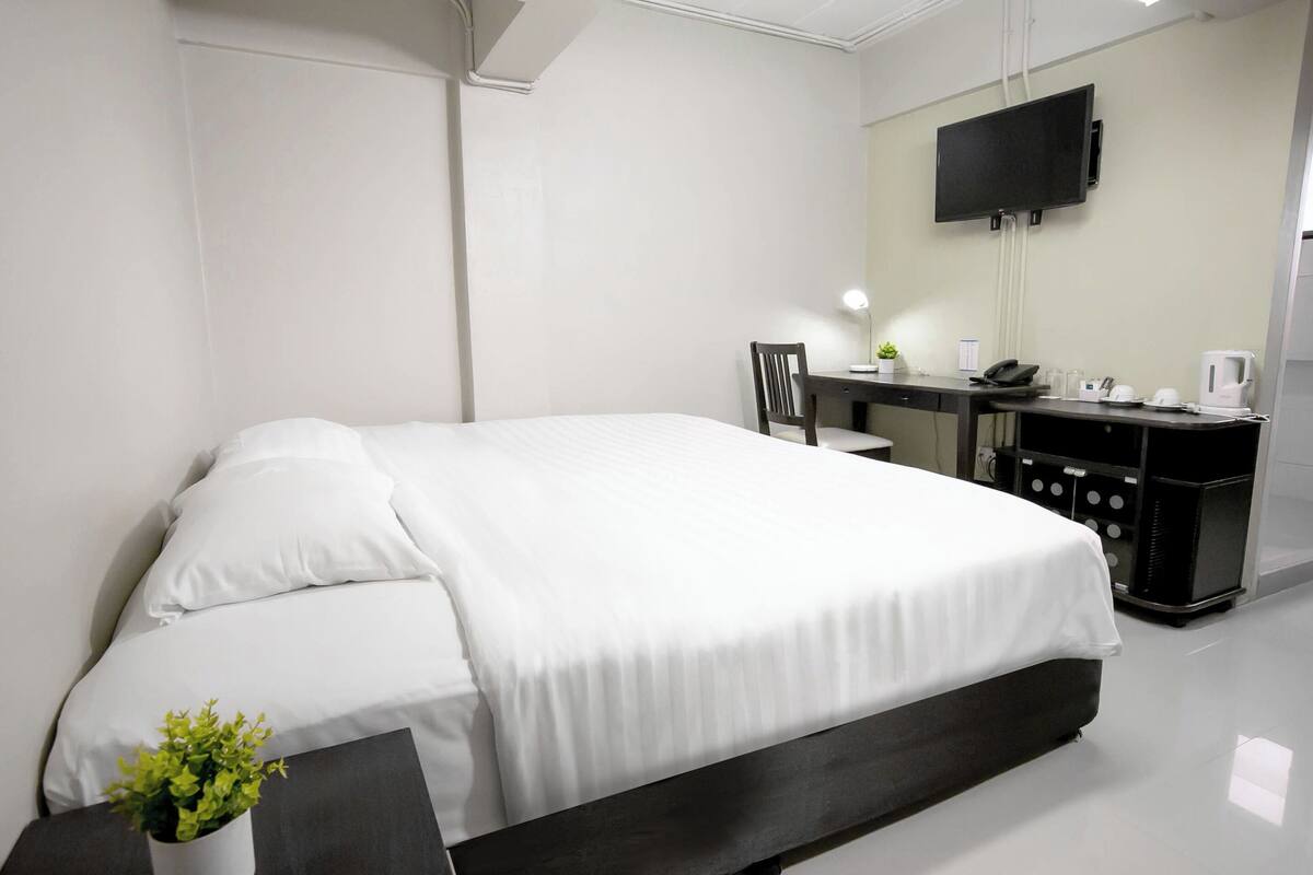 A modern hotel room with a large bed, a desk with a chair, a flat-screen TV, and a coffee machine.