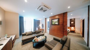 A hotel room with a living area featuring a sofa set, a coffee table with floral arrangement, a desk with a lamp, and a painting on the wall. - Petro Hotel (Ho Chi Minh City)