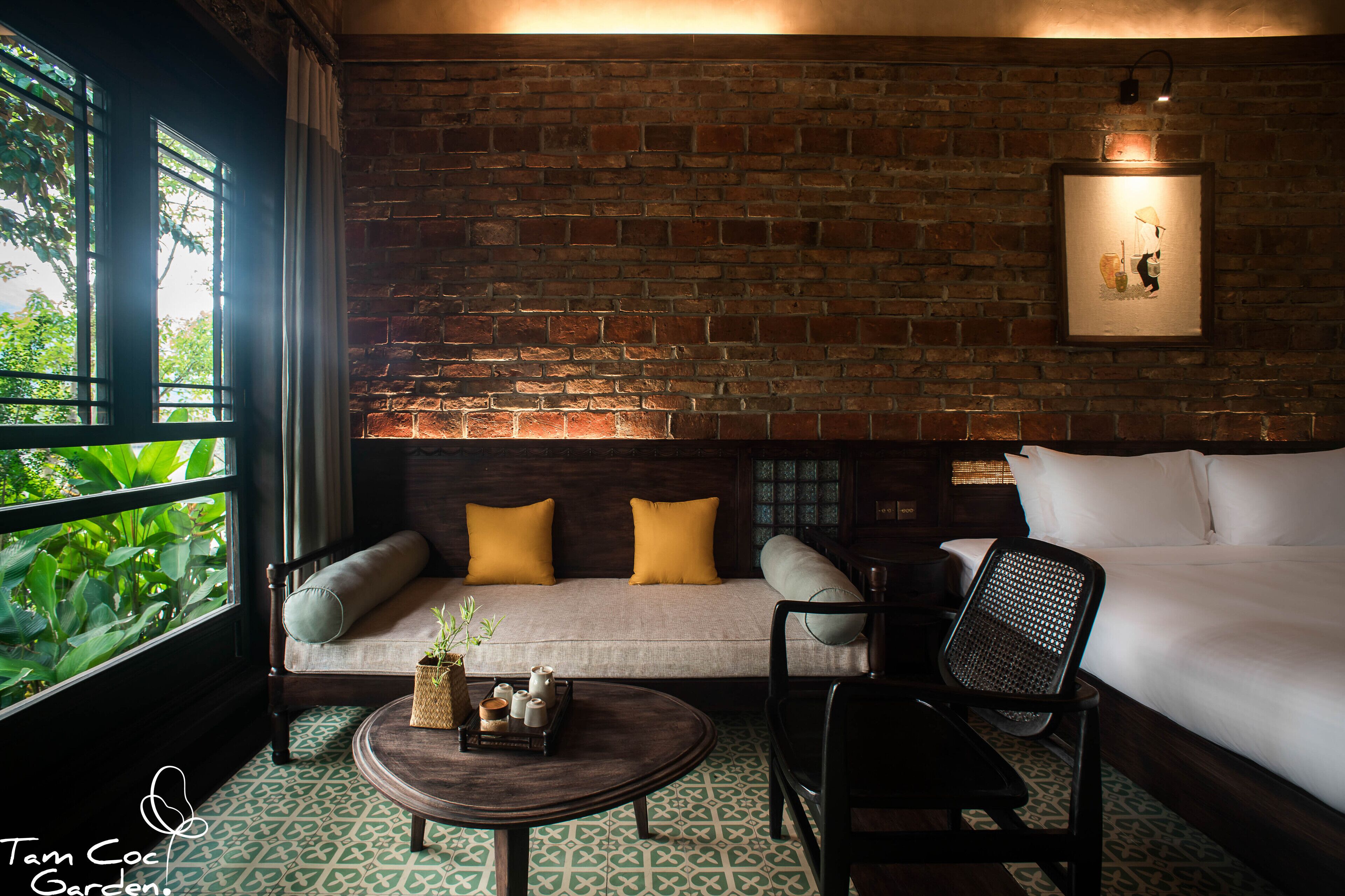 A cozy room with a brick wall, a sofa with cushions, a bed, a chair, and a small table with a tray.