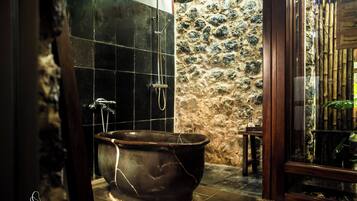 A bathroom with a freestanding bathtub, a shower, and a stone wall.