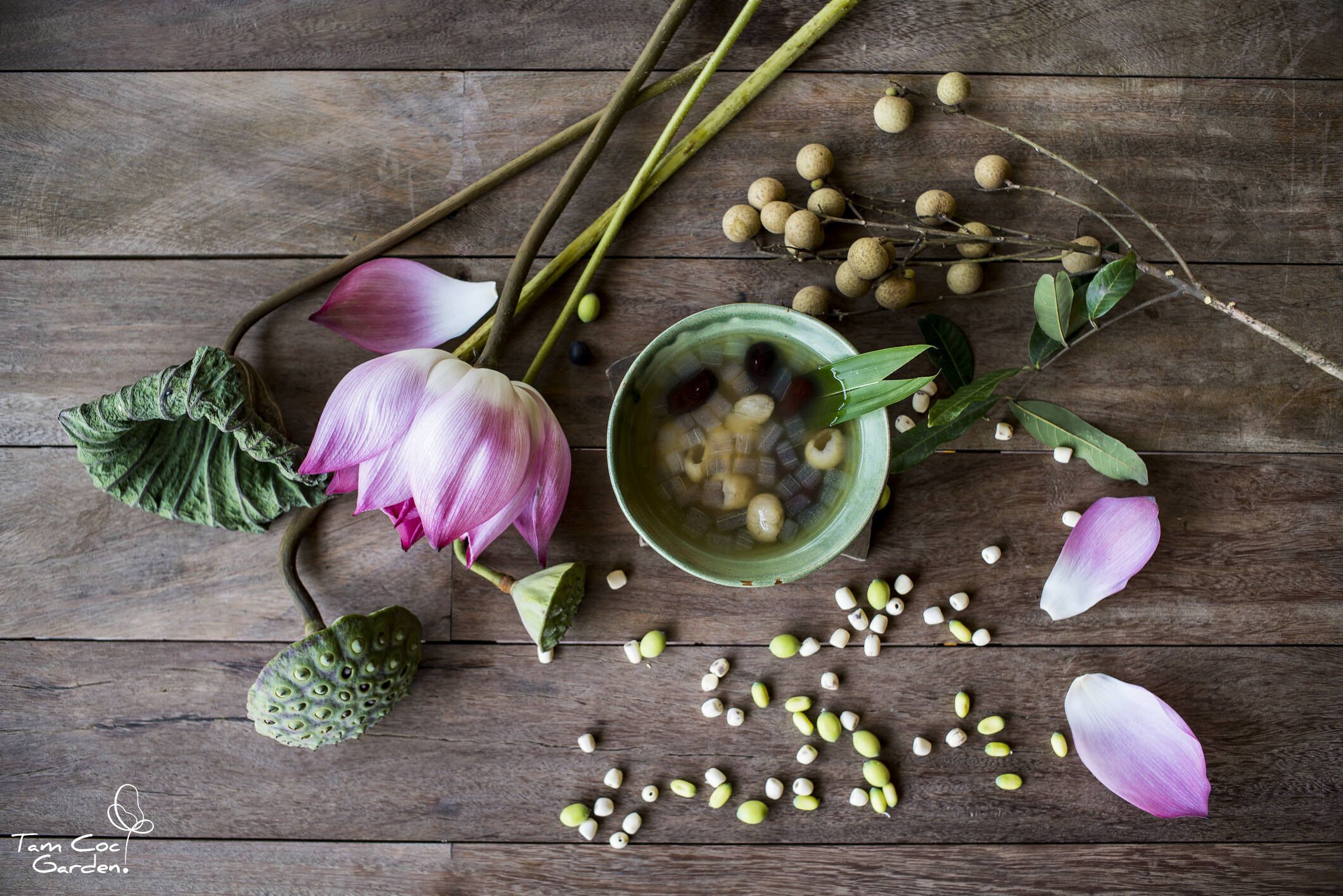 A wooden surface with a lotus flower, green leaves, and a bowl of seeds.