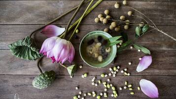 A wooden surface with a lotus flower, green leaves, and a bowl of seeds.