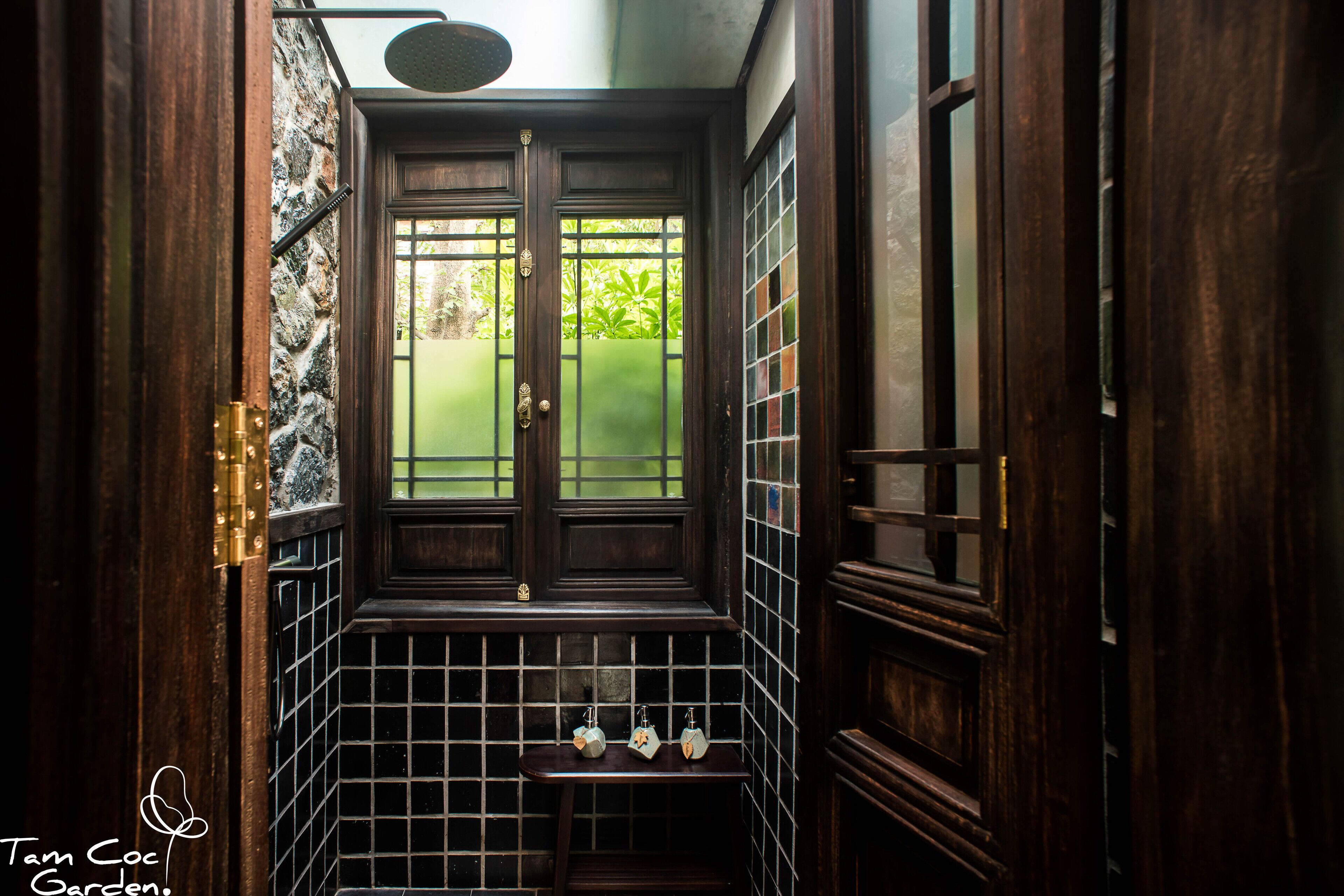 Un couloir étroit et sombre, avec un sol carrelé et des murs en bois, une petite étagère sur laquelle sont posés trois objets décoratifs, et une porte dotée d’une fenêtre.