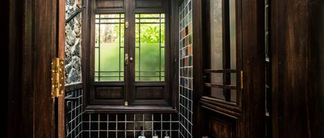 A narrow, dark wooden hallway with a tiled floor, a small shelf with three decorative items, and a door with a window.