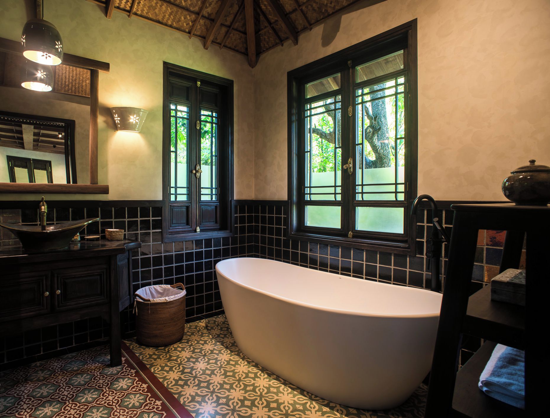 A bathroom with a freestanding bathtub, a sink with a mirror above it, and a window with a view of greenery outside.