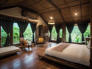 Un dormitorio amplio con una cama grande, suelo de madera y vistas a exuberante vegetación.