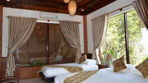 Una habitación con dos camas, una pared de ladrillo y amplios ventanales con cortinas.