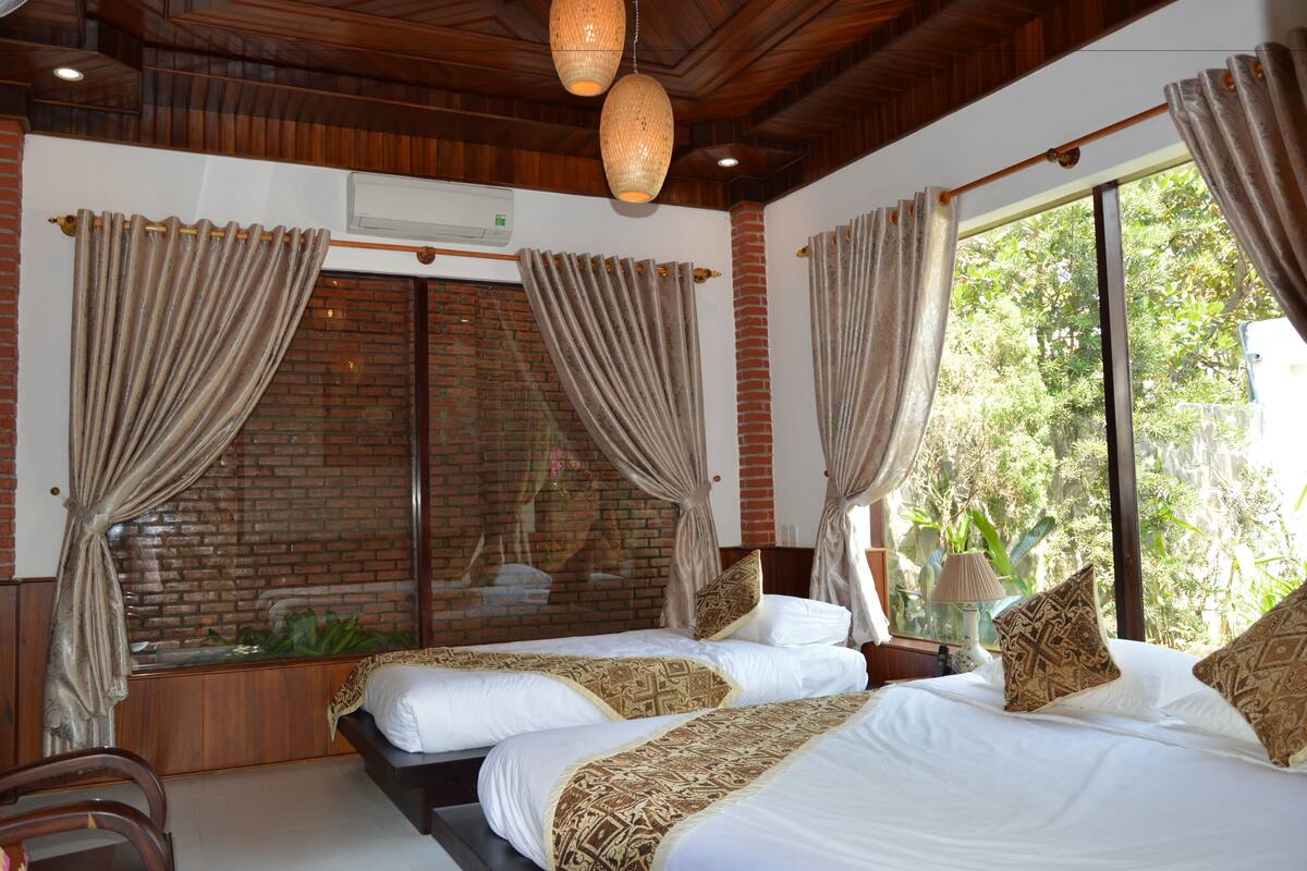 A room with two beds, a brick wall, and large windows with curtains.