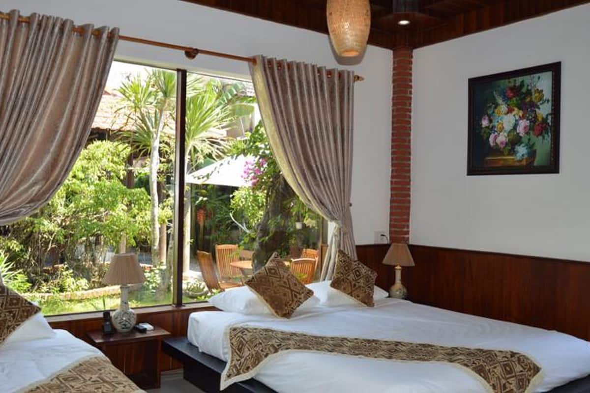 A hotel room with a large window, a bed with patterned bedding, a bedside table with a lamp, and a painting on the wall.