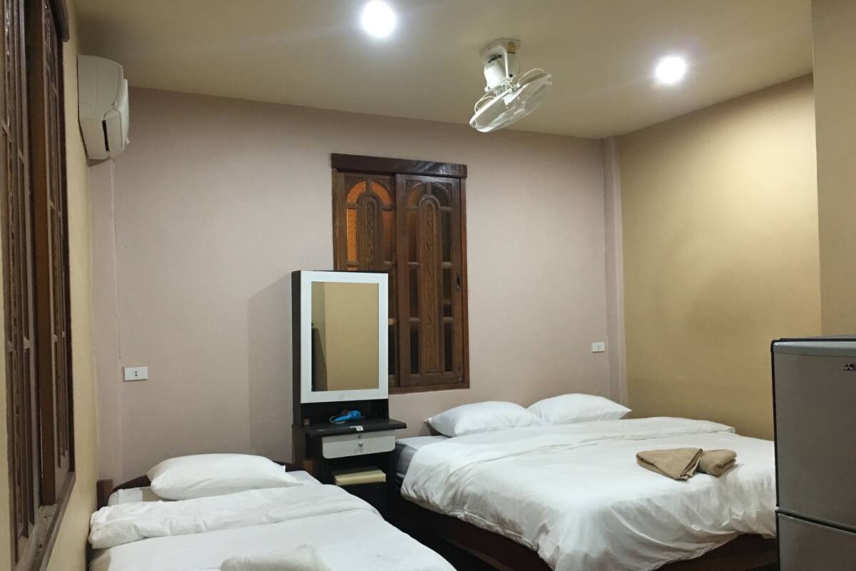 A hotel room with two beds, a television, a mirror, and a ceiling fan.