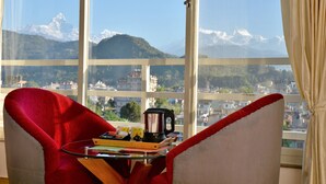 Une pièce dotée d’une grande fenêtre donnant sur les montagnes, d’un fauteuil rouge, d’une petite table avec une bouilloire et un plateau.
