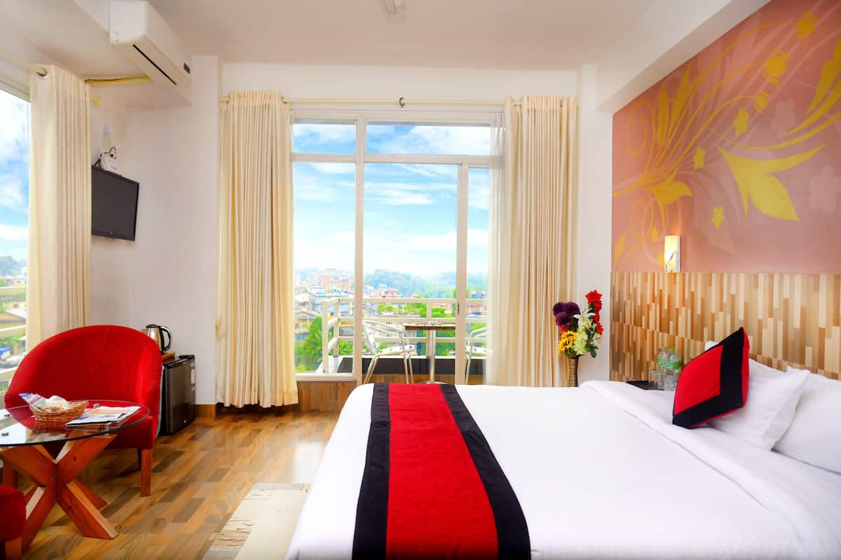 A hotel room with a large bed, a desk with a chair, a TV, and a balcony with a view of the city.