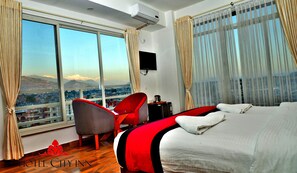 Habitación de hotel con una ventana grande, una cama, una silla, un escritorio y un televisor.