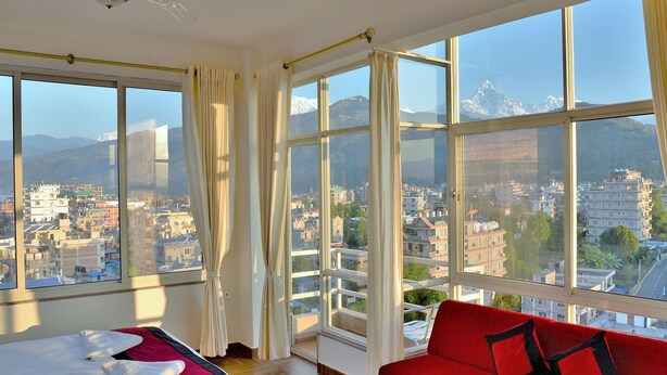 Une chambre d’hôtel avec un lit, un canapé rouge et de grandes fenêtres donnant sur la ville.