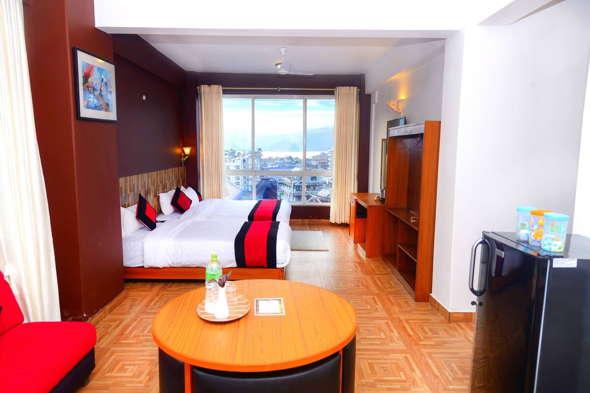 A hotel room with a bed, a dining table, a refrigerator, and a view of the city.
