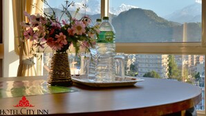 Une table avec un vase de fleurs, une bouteille d’eau et un pichet en verre, placée près d’une fenêtre donnant sur une vue sur les montagnes.
