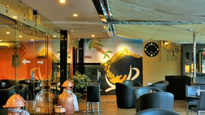 Un espace de détente intérieur moderne, doté de tables rondes et de chaises noires, et agrémenté d’une fresque représentant une montagne et une main.