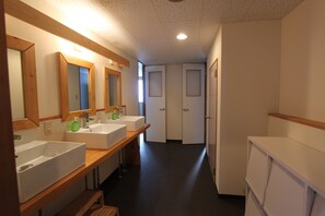 A hotel bathroom with two sinks, wooden benches, and a mirror. - Alpine Villa Nozawa (Nozawaonsen)