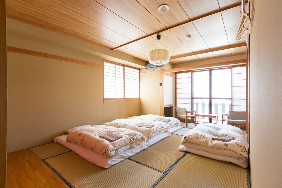 A traditional Japanese room with tatami flooring, a futon bed, sliding doors, and a view of the outside.