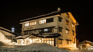 A multi-story hotel with a traditional architectural style, featuring large windows and a snow-covered ground. - Alpine Villa Nozawa (Nozawaonsen)