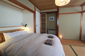 A neatly made bed with pillows and towels, a bedside lamp, a small shelf, and a picture on the wall. - Alpine Villa Nozawa (Nozawaonsen)