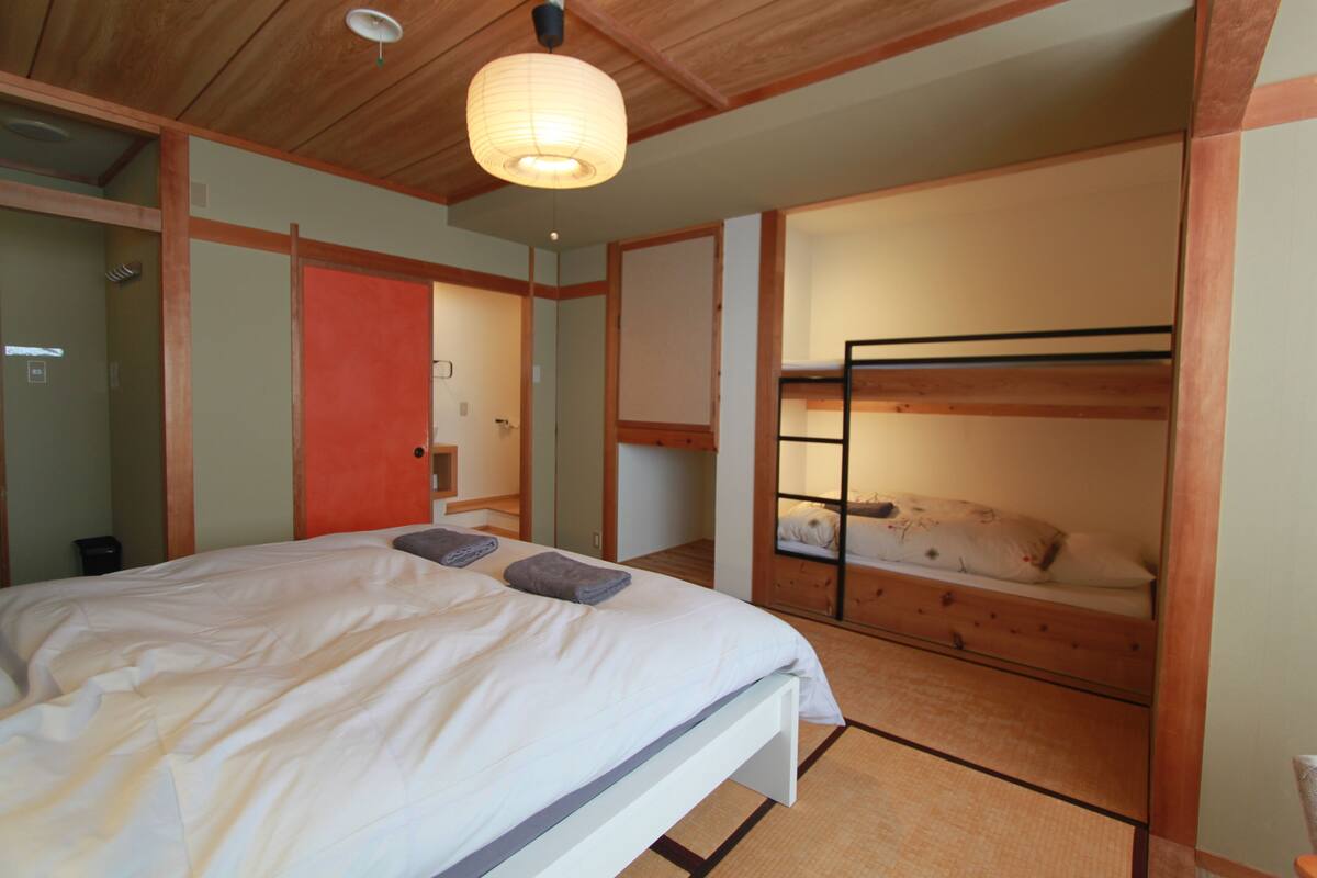 A bedroom with a bunk bed, a large bed with pillows, and a wooden ceiling.