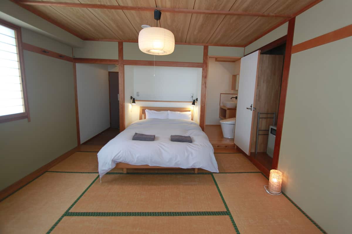 A traditional Japanese-style bedroom with tatami flooring, a wooden bed frame, a nightstand, a washbasin, and a hanging lamp.