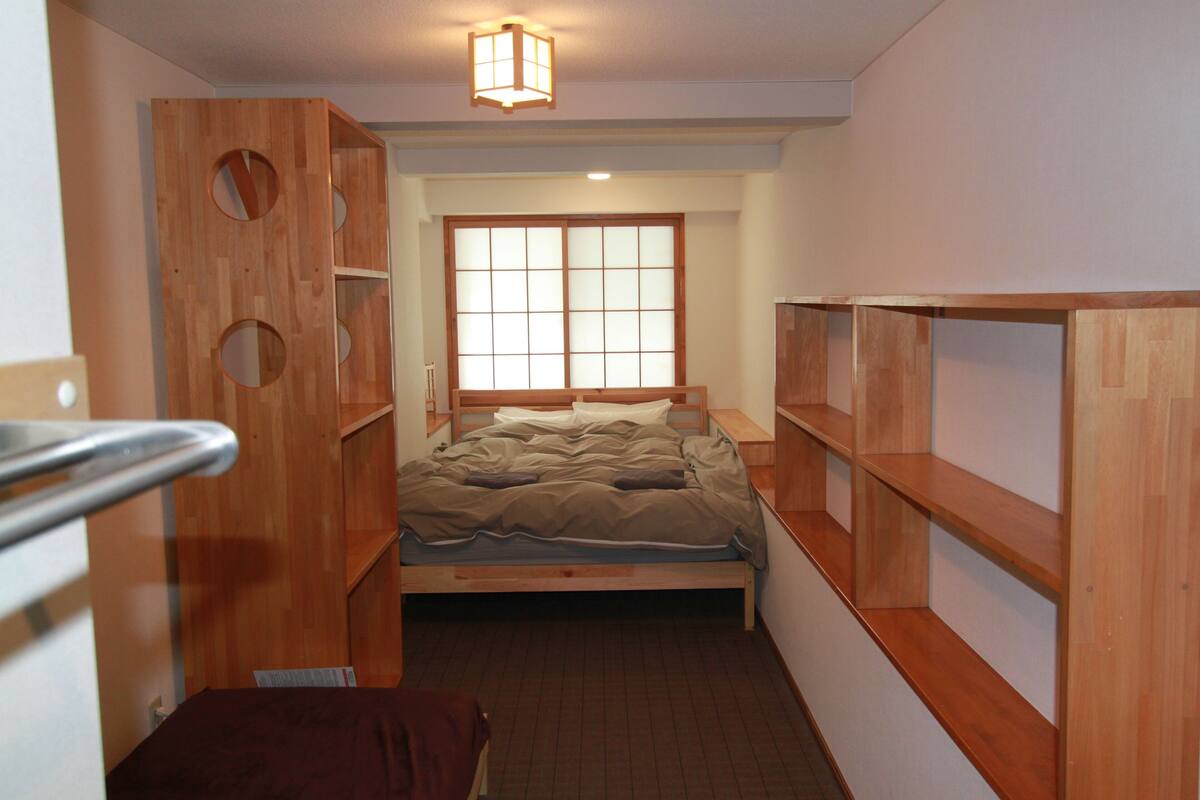A compact room with a bed, wooden shelving, and a window with a view.