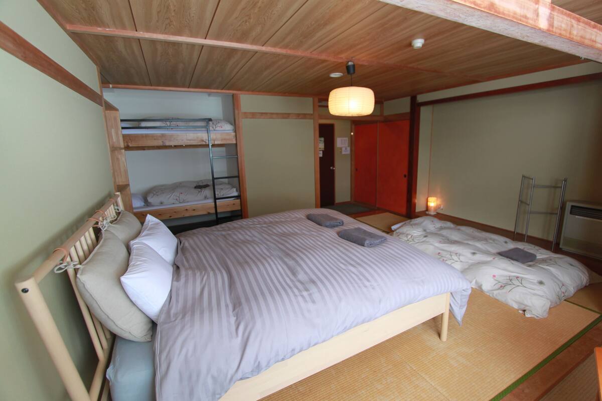 A room with a bunk bed, a single bed, tatami mats, a hanging light fixture, and a sliding door.