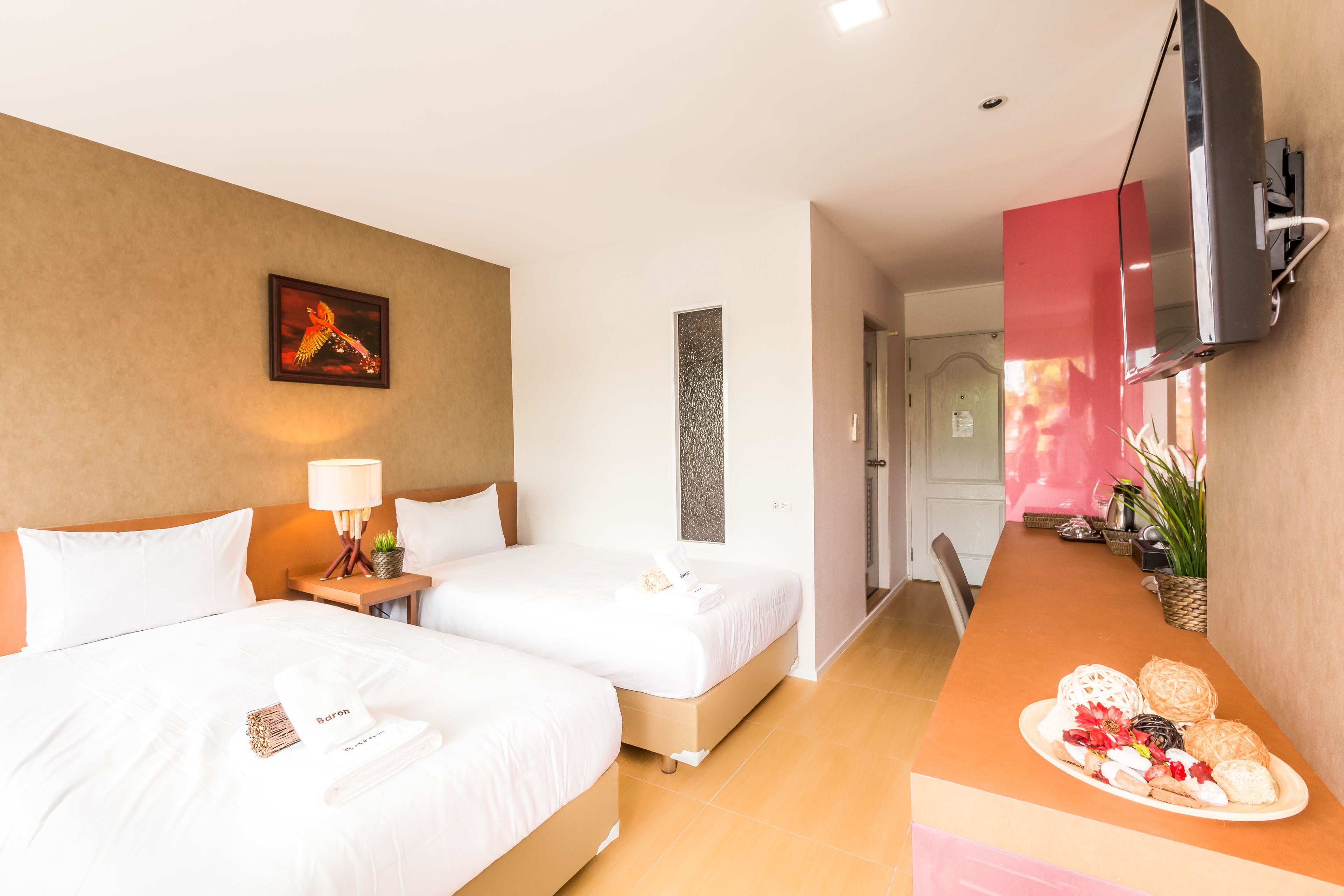 A hotel room with two beds, a TV mounted on the wall, a breakfast tray on the counter, and a painting on the wall.