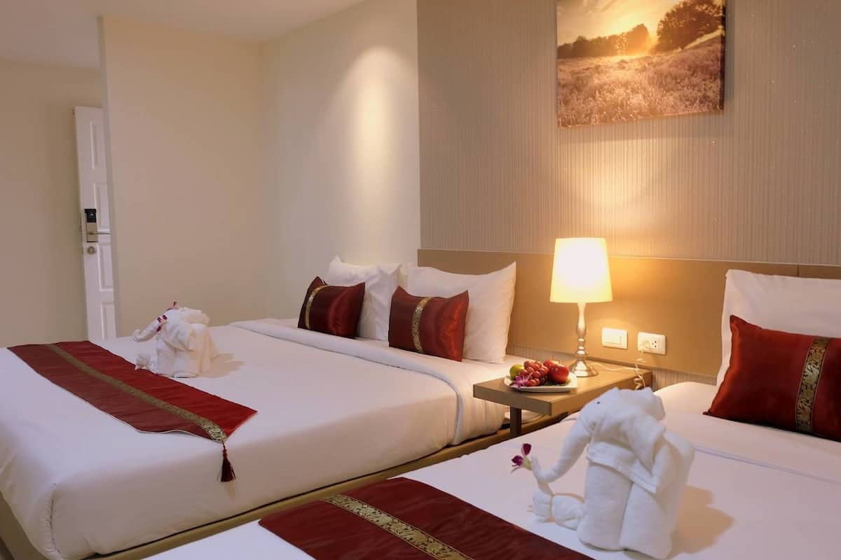 A hotel room with two beds, each with white linens and red pillows, a bedside table with a lamp, and a painting on the wall.