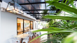 An outdoor dining area with glass tables and white chairs, surrounded by plants and a modern architectural design. - Baron Residence Bangkok (Bangkok)