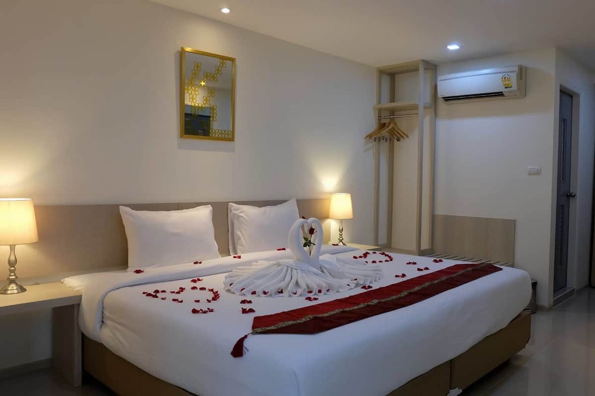 A hotel room with a neatly made bed, two bedside lamps, a mirror, an air conditioning unit, and a chair.