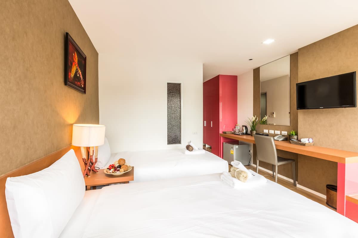 A hotel room with two beds, a desk, a TV, and a bathroom.