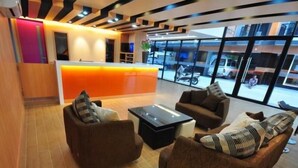 A modern lobby with a reception desk, seating area with sofas and a coffee table, and large windows offering a view of the street. - Baron Residence Bangkok (Bangkok)