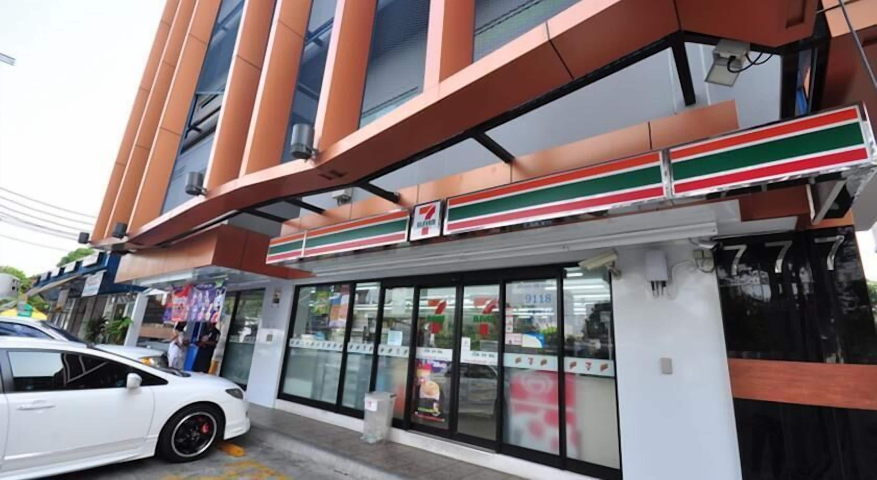 A 7-Eleven convenience store with a modern facade, large windows, and a white car parked in front.