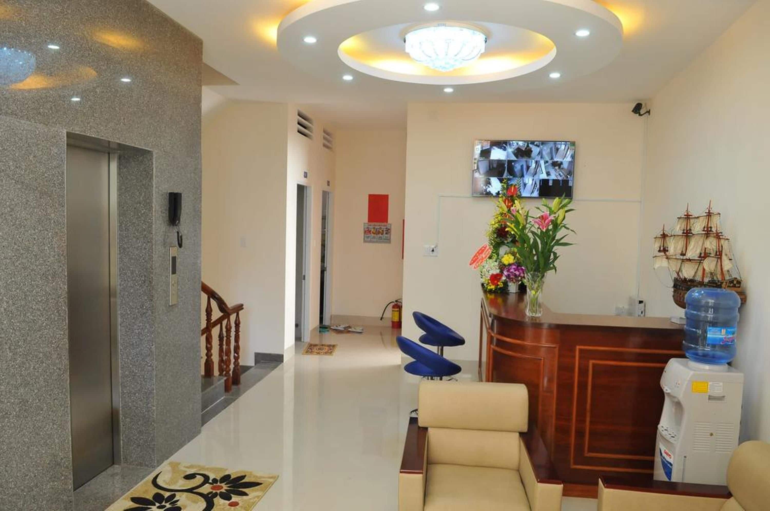 A hotel lobby with a reception desk, a television mounted on the wall, a water dispenser, and a decorative ship model.